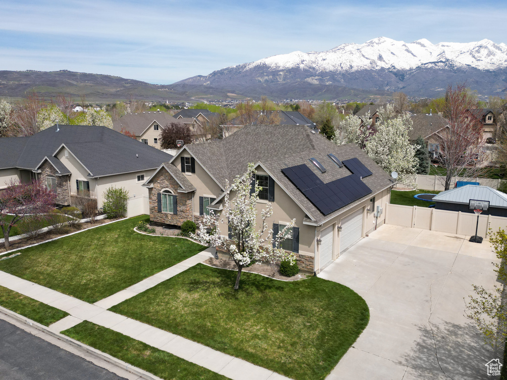 View of front of home featuring solar panels, a mountain view, a garage, and a front lawn