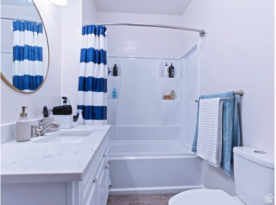 Full bathroom with hardwood / wood-style floors, oversized vanity, shower / tub combo, and toilet