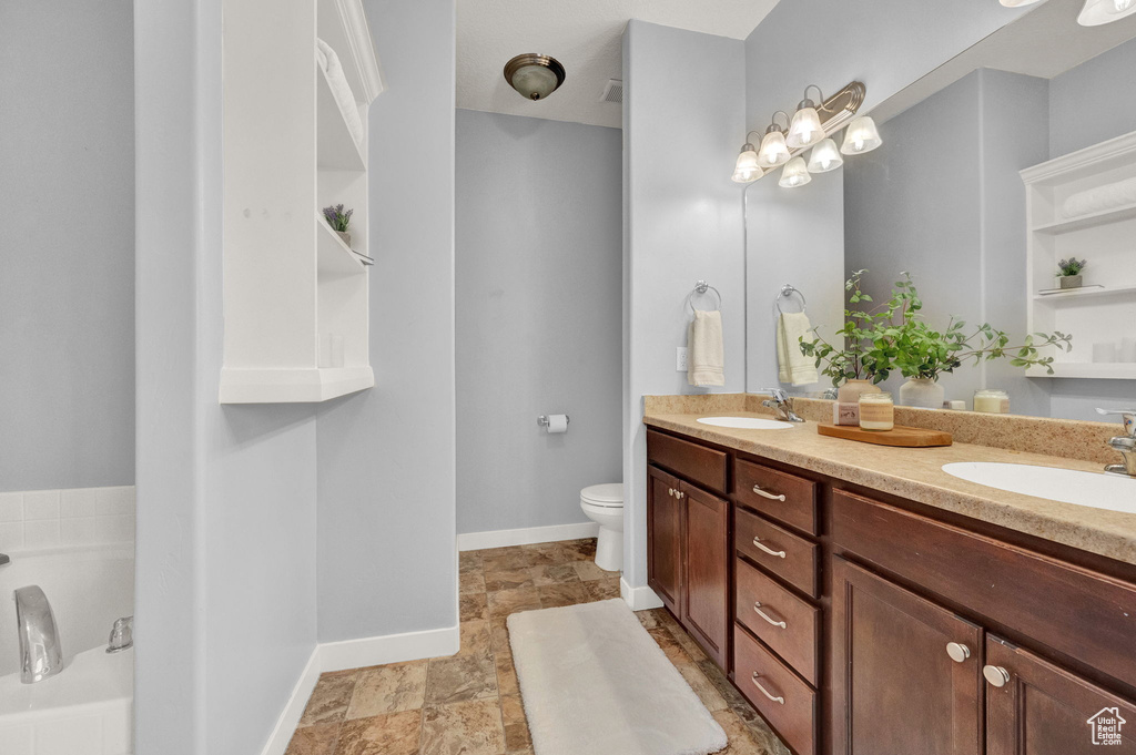 Bathroom featuring tile flooring, toilet, dual vanity, and a bathtub