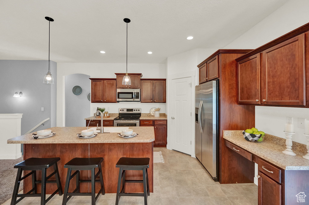 Kitchen with appliances with stainless steel finishes, light tile floors, a breakfast bar area, hanging light fixtures, and an island with sink