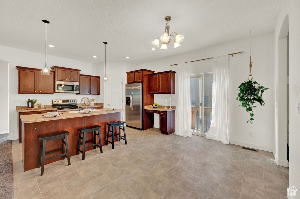 Kitchen featuring pendant lighting, light tile flooring, a kitchen breakfast bar, stainless steel appliances, and a kitchen island with sink