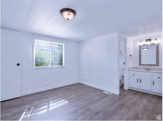 Unfurnished bedroom featuring hardwood / wood-style floors, ensuite bathroom, and a textured ceiling