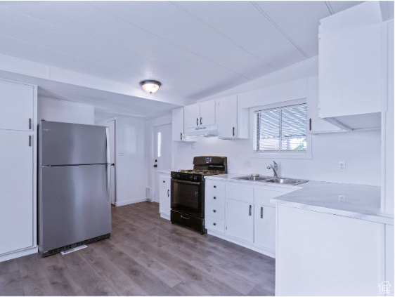 Kitchen featuring white cabinets, electric range oven, wood-type flooring, and stainless steel refrigerator