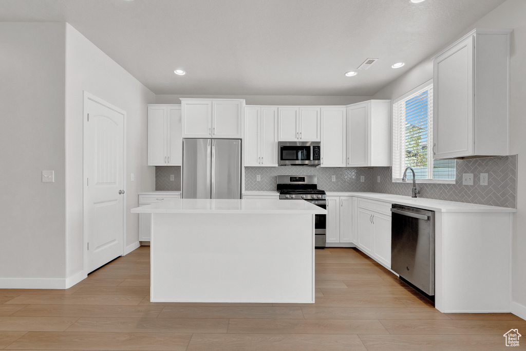 Kitchen featuring a kitchen island, backsplash, white cabinetry, and stainless steel appliances