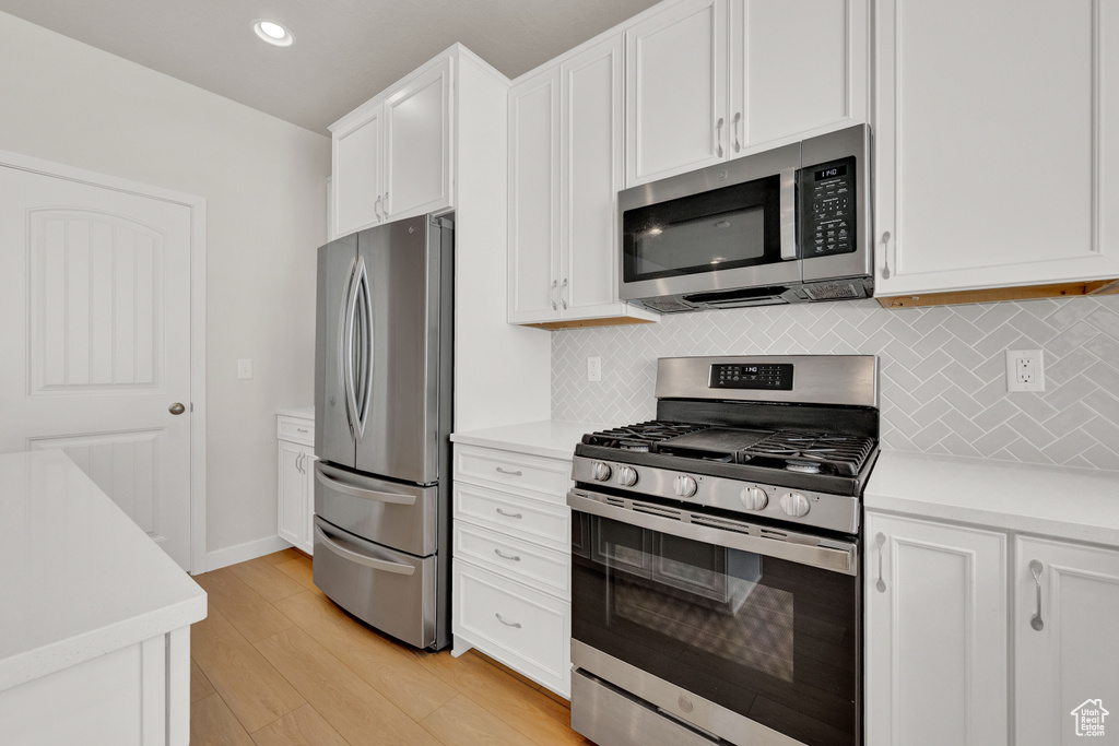 Kitchen with appliances with stainless steel finishes, tasteful backsplash, light hardwood / wood-style floors, and white cabinetry