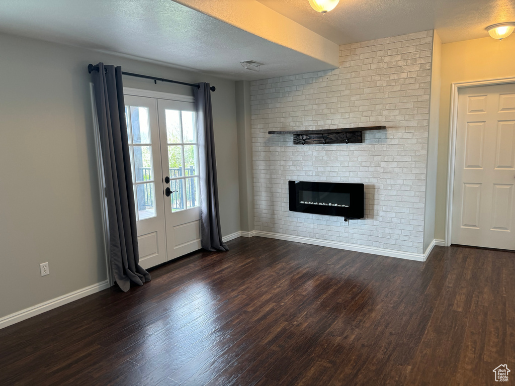 Unfurnished living room with french doors, brick wall, a textured ceiling, dark wood-type flooring, and a fireplace
