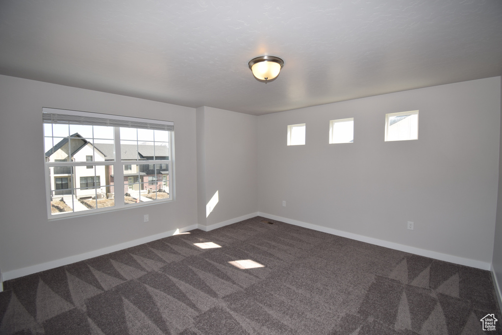 Empty room with plenty of natural light and dark colored carpet