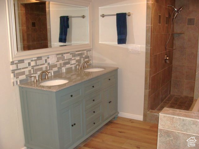 Bathroom with dual bowl vanity, tiled shower, tasteful backsplash, and hardwood / wood-style floors