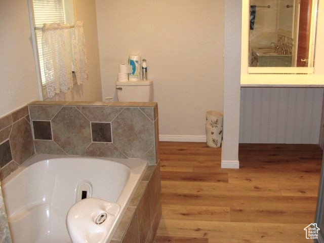 Bathroom with a relaxing tiled bath, toilet, and hardwood / wood-style floors