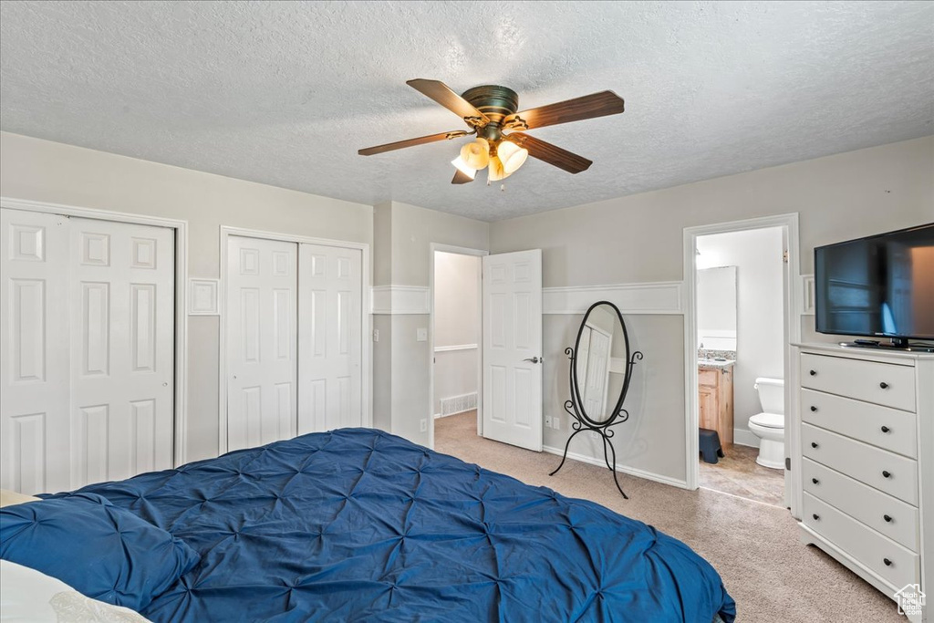Carpeted bedroom featuring connected bathroom, ceiling fan, a textured ceiling, and multiple closets