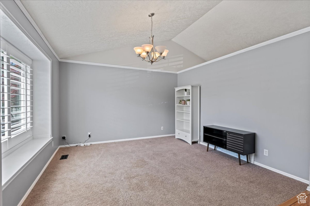 Unfurnished room with carpet floors, ornamental molding, an inviting chandelier, vaulted ceiling, and a textured ceiling