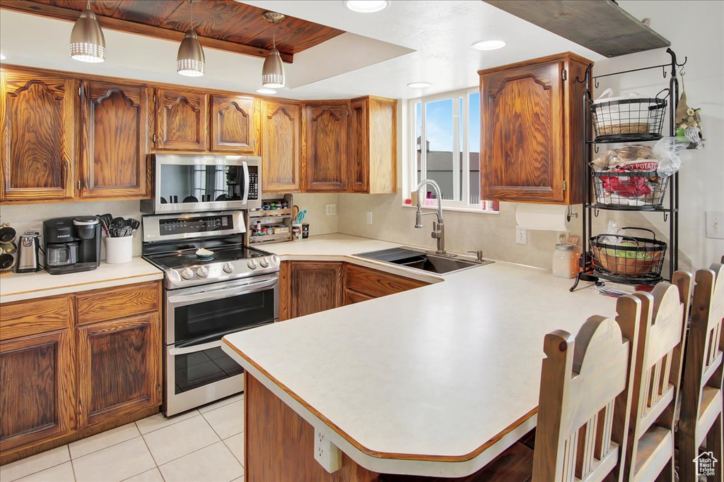 Kitchen featuring kitchen peninsula, stainless steel appliances, light tile flooring, sink, and a raised ceiling