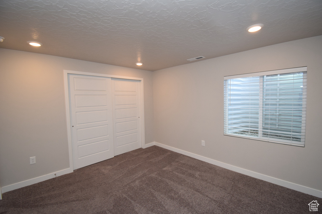 Unfurnished bedroom featuring dark colored carpet, a closet, and a textured ceiling