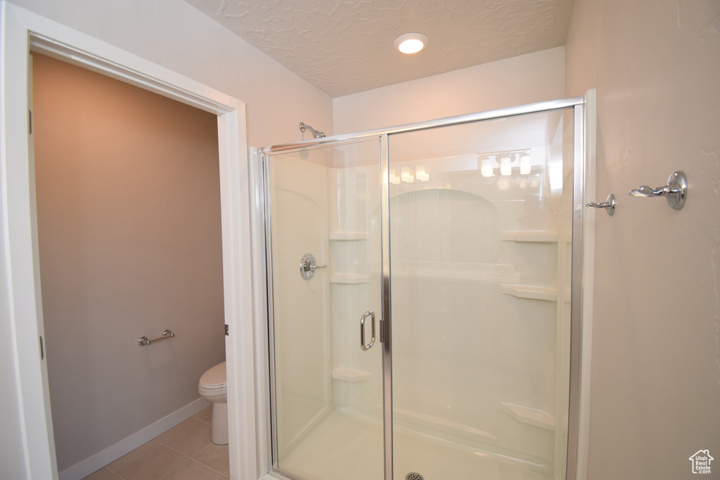 Bathroom with a textured ceiling, a shower with shower door, tile floors, and toilet