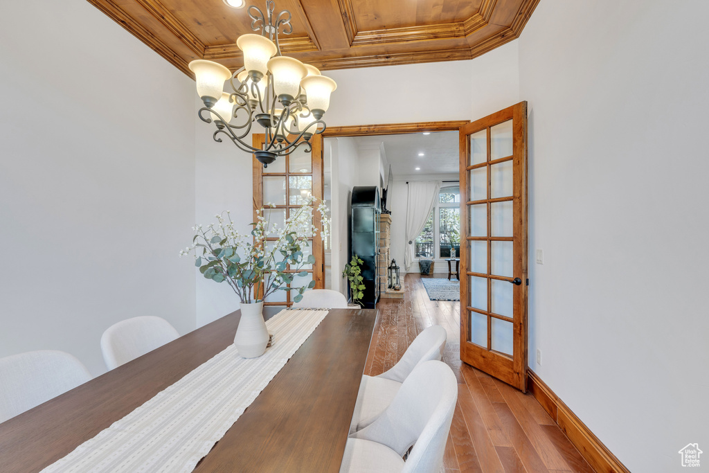 Dining area featuring light wood-type flooring, french doors, crown molding, wooden ceiling, and a notable chandelier