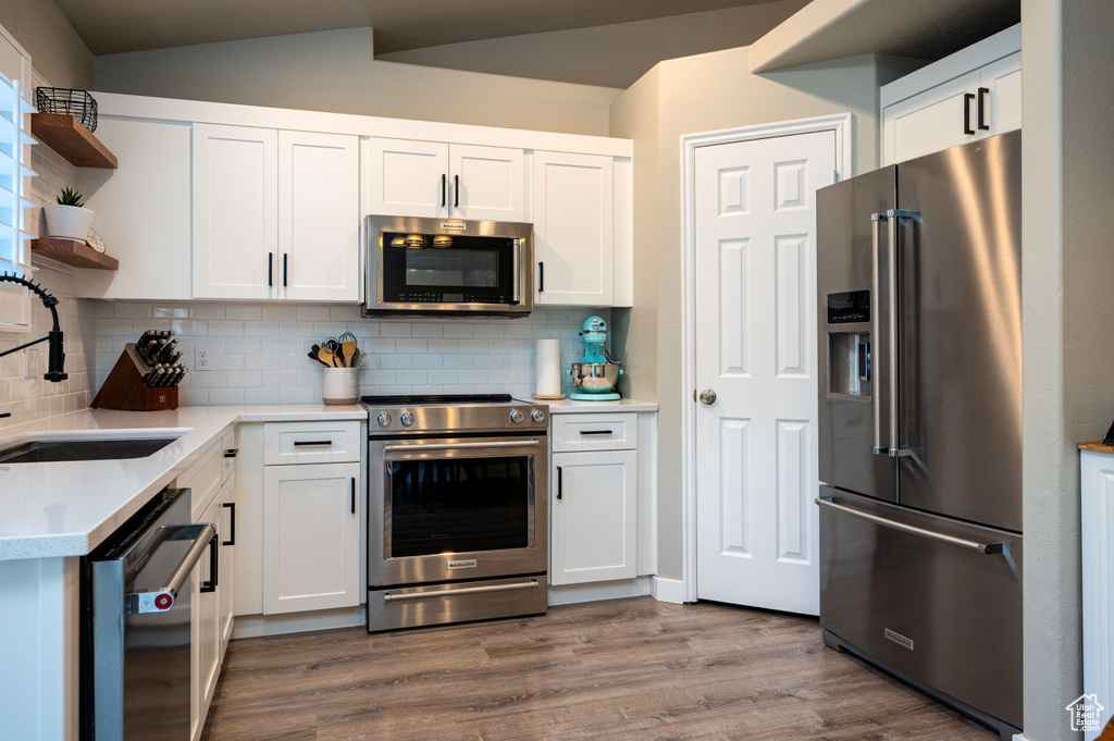 Kitchen with stainless steel appliances, tasteful backsplash, dark wood-type flooring, white cabinets, and sink