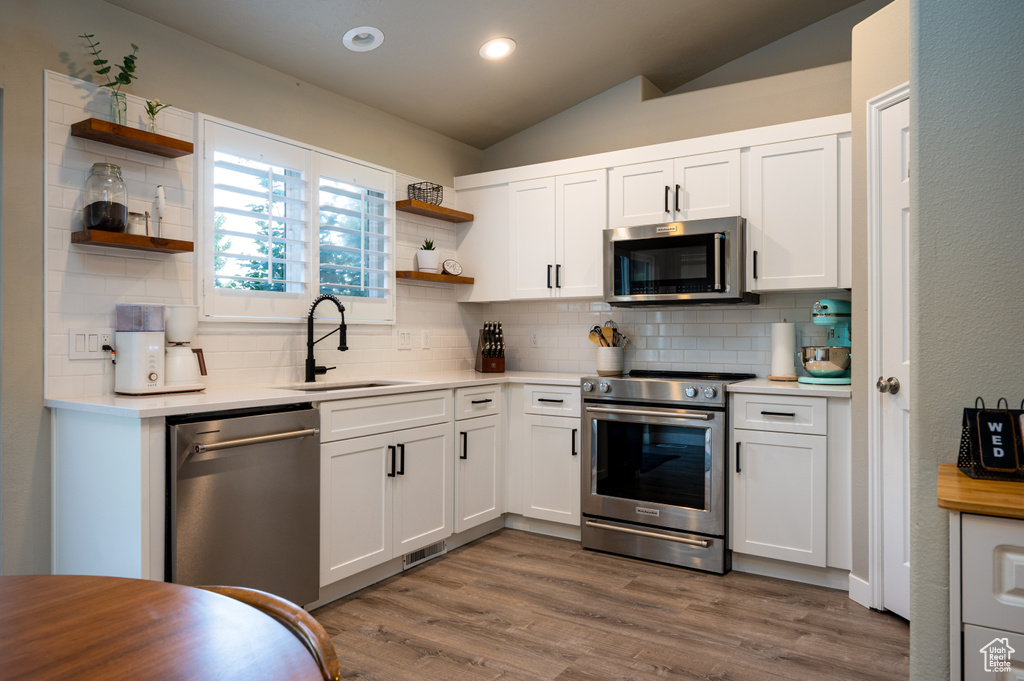 Kitchen featuring white cabinets, hardwood / wood-style floors, backsplash, stainless steel appliances, and sink
