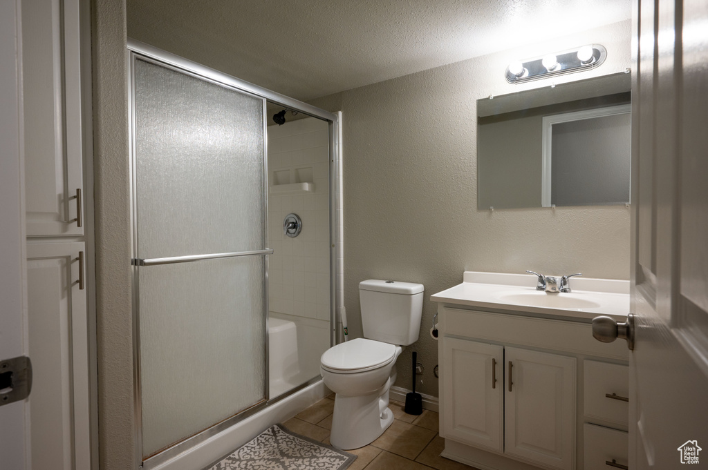 Bathroom featuring walk in shower, vanity, tile flooring, toilet, and a textured ceiling