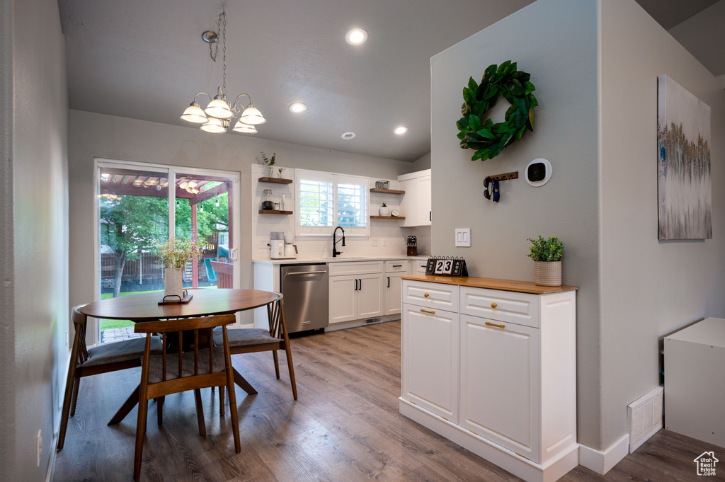 Kitchen featuring decorative light fixtures, backsplash, dishwasher, white cabinets, and light wood-type flooring