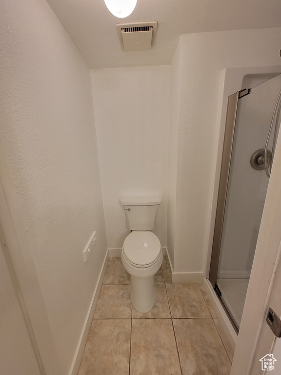 Bathroom with tile flooring, a shower with door, and toilet