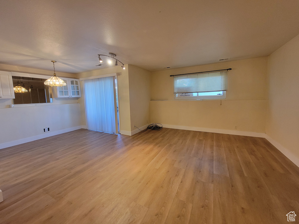 Empty room with hardwood / wood-style flooring, rail lighting, and a notable chandelier