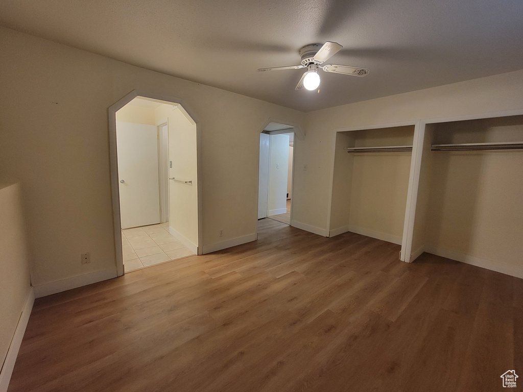 Unfurnished bedroom with light hardwood / wood-style floors, ceiling fan, and two closets