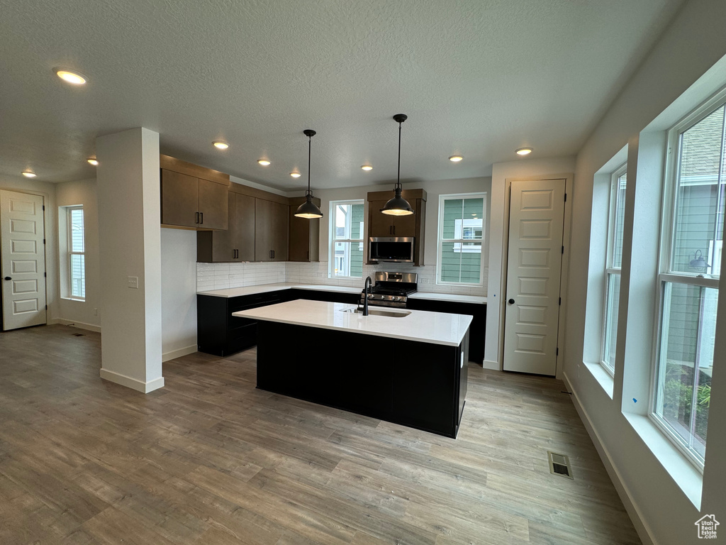 Kitchen with stainless steel appliances, hardwood / wood-style flooring, an island with sink, dark brown cabinetry, and pendant lighting