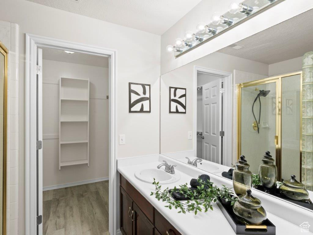 Bathroom featuring wood-type flooring, vanity with extensive cabinet space, a shower with shower door, and a textured ceiling