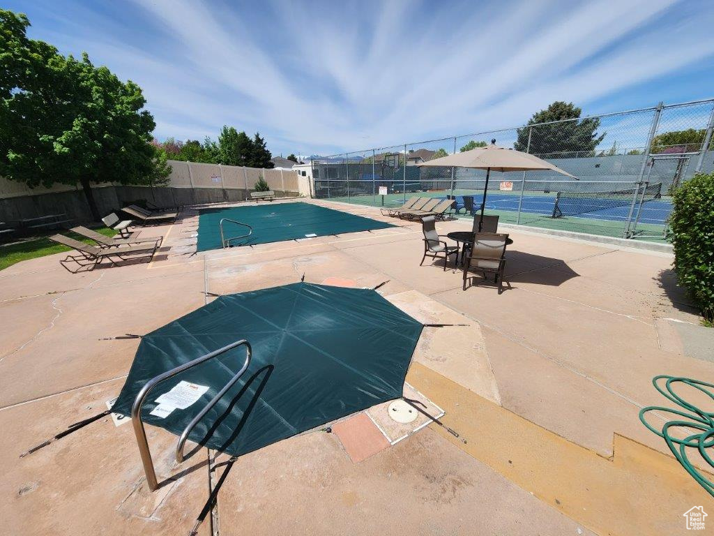 View of swimming pool with tennis court and a patio area