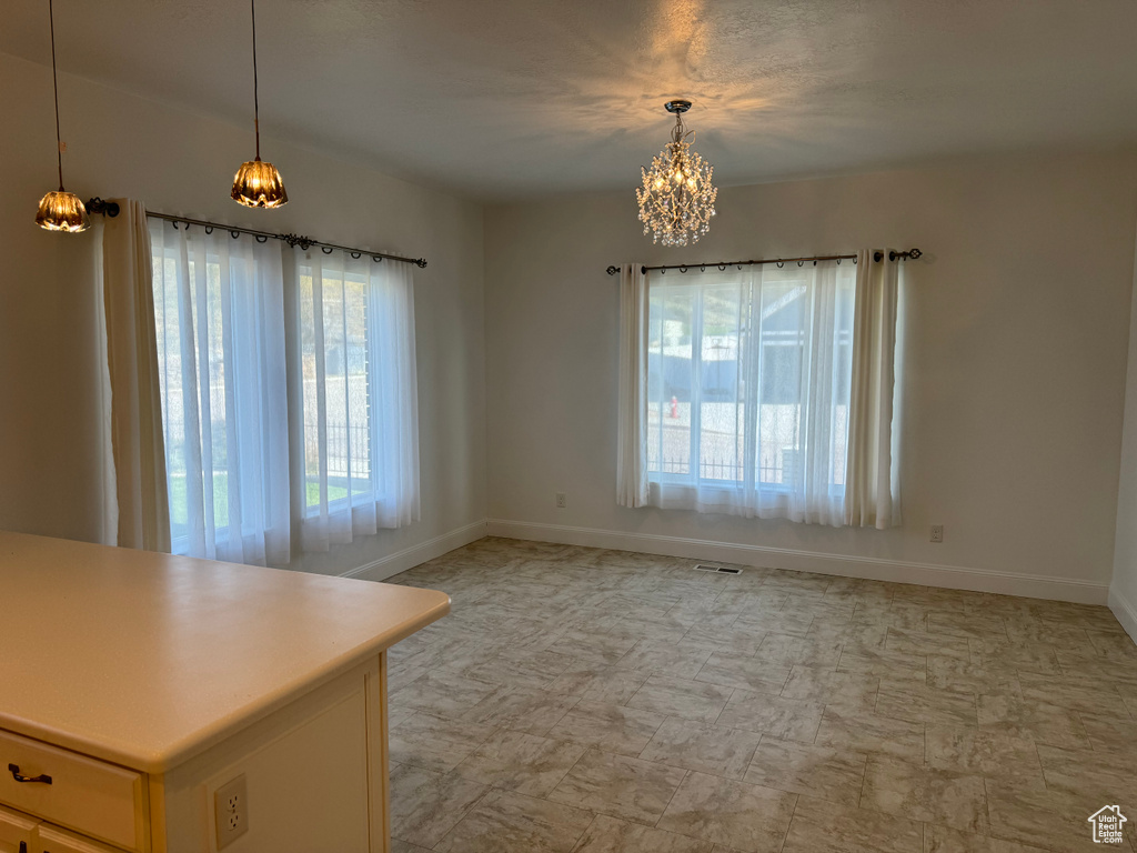 Empty room with a wealth of natural light, a notable chandelier, and light tile floors