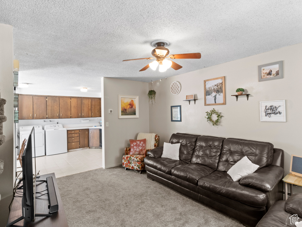 Carpeted living room featuring a textured ceiling, ceiling fan, and washing machine and dryer