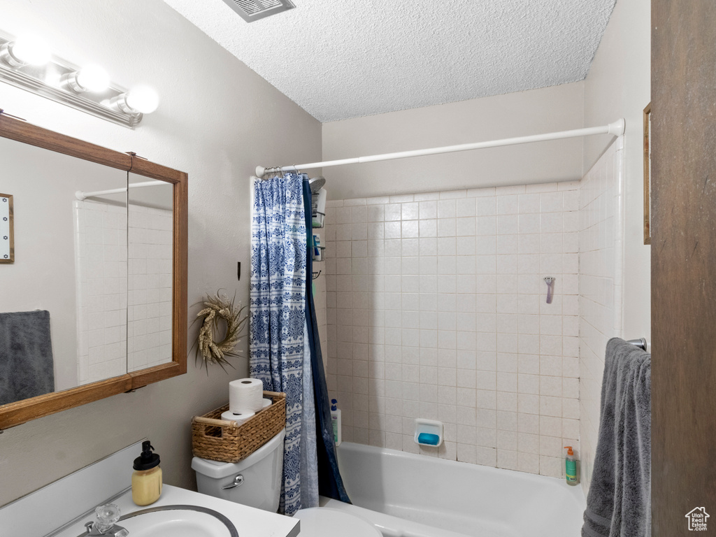 Full bathroom with sink, toilet, shower / tub combo with curtain, and a textured ceiling