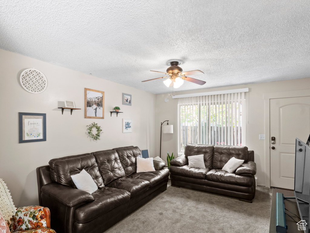Living room with a textured ceiling, carpet floors, and ceiling fan
