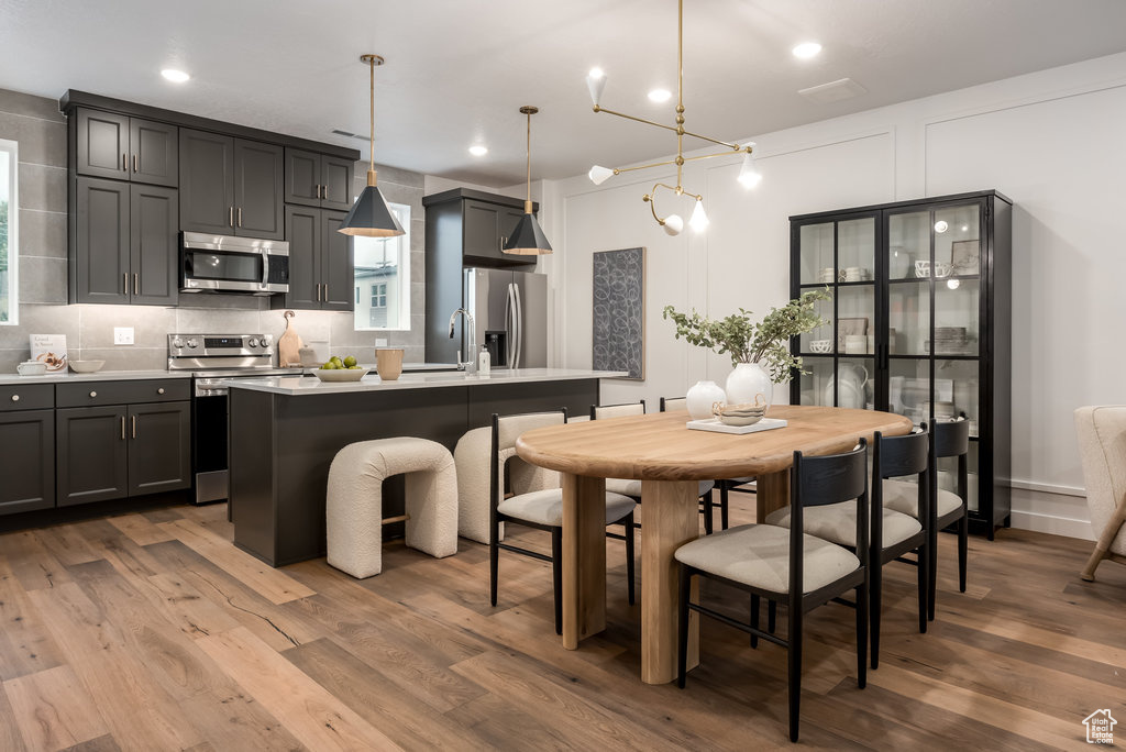 Kitchen featuring tasteful backsplash, hardwood / wood-style floors, hanging light fixtures, stainless steel appliances, and a kitchen island with sink
