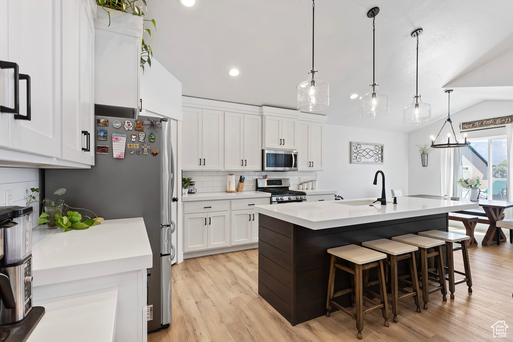Kitchen with appliances with stainless steel finishes, white cabinets, sink, light hardwood / wood-style floors, and a kitchen island with sink