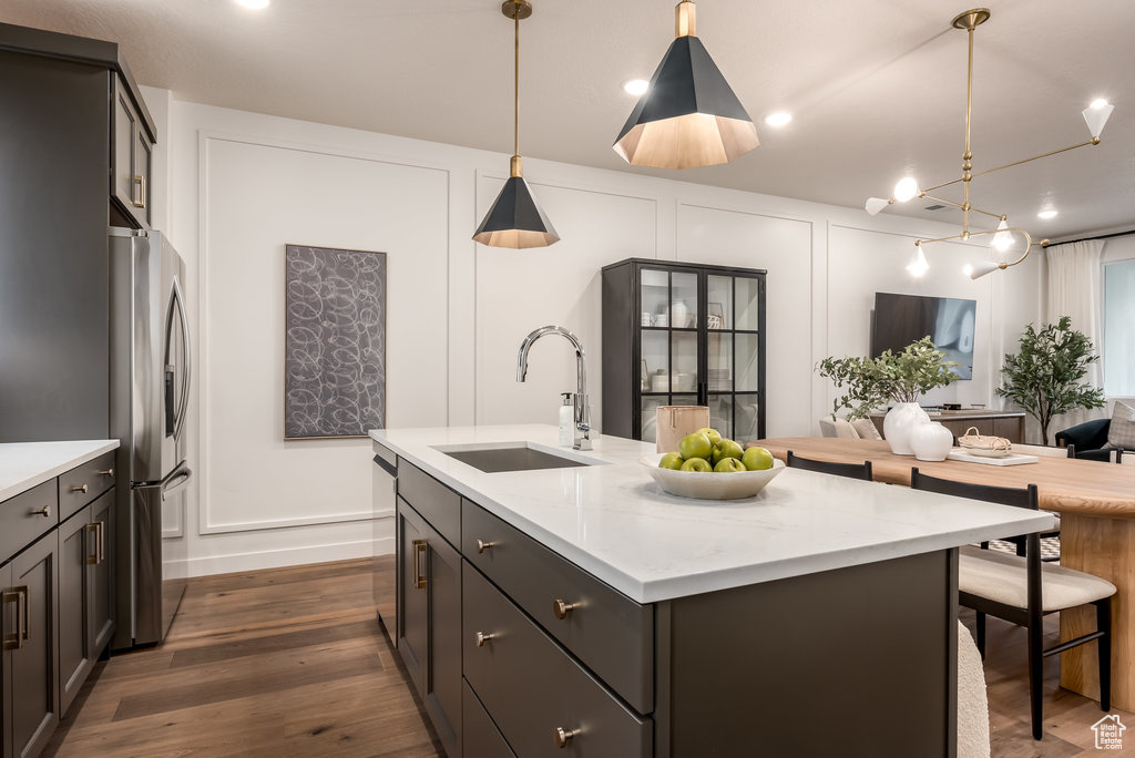 Kitchen featuring hanging light fixtures, appliances with stainless steel finishes, a center island with sink, dark wood-type flooring, and sink