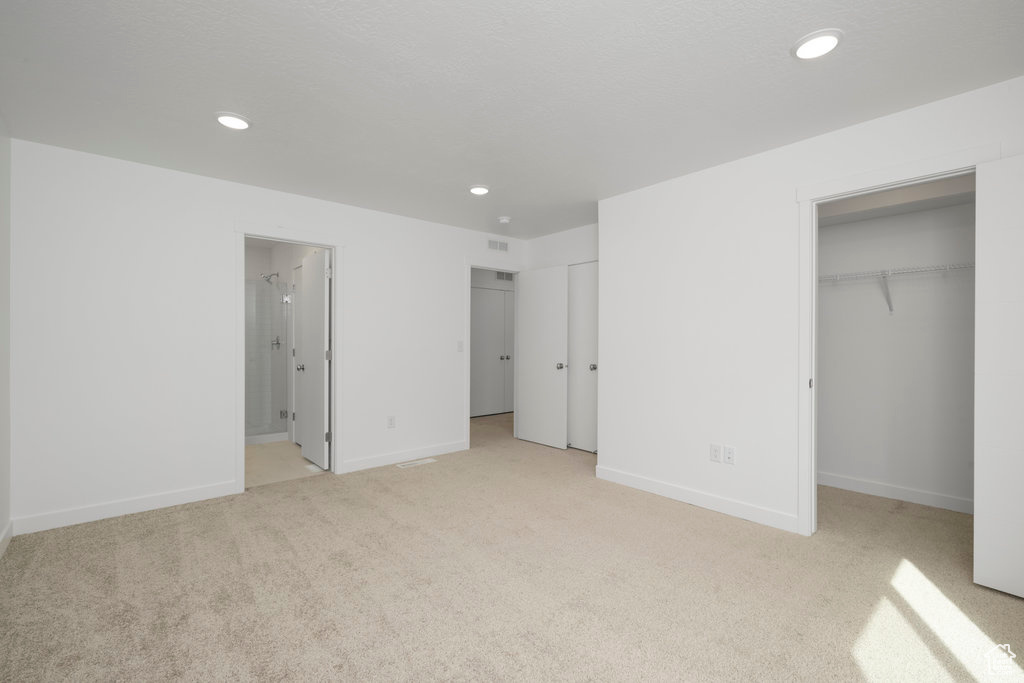 Unfurnished bedroom with light colored carpet, a walk in closet, ensuite bath, and a closet