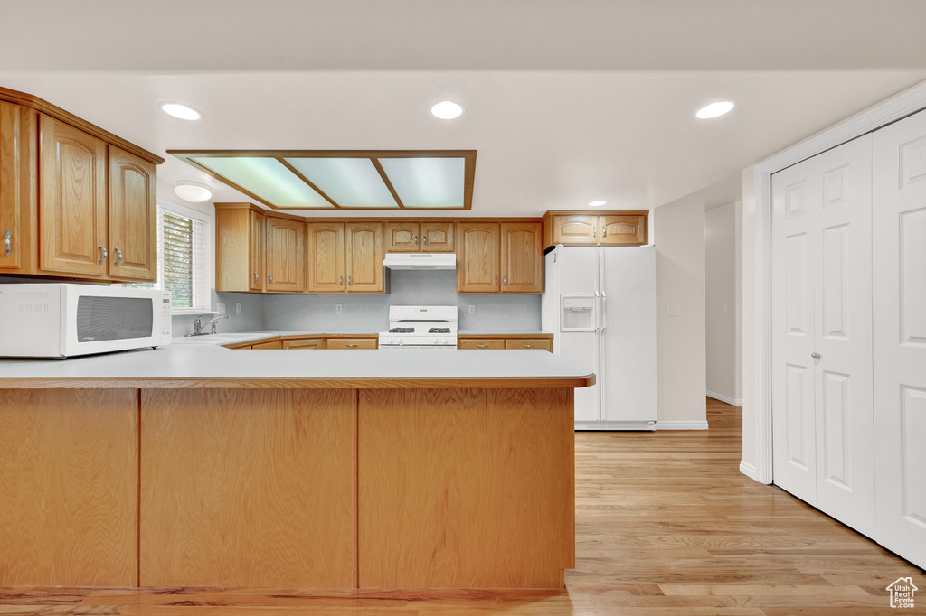 Kitchen featuring light hardwood / wood-style flooring, white appliances, kitchen peninsula, and sink