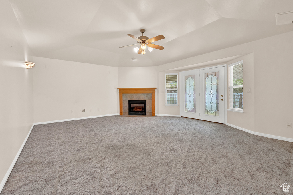 Unfurnished living room featuring ceiling fan, carpet, a tiled fireplace, vaulted ceiling, and french doors