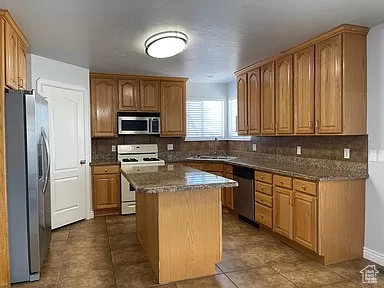 Kitchen featuring a center island, tile floors, backsplash, stainless steel appliances, and sink