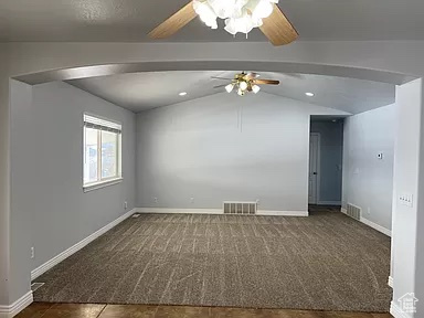 Empty room featuring dark colored carpet, ceiling fan, and vaulted ceiling