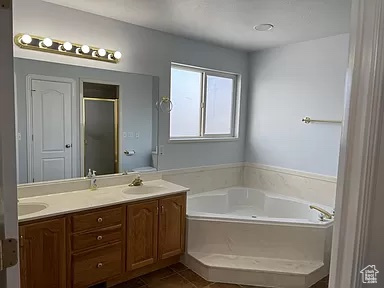 Bathroom featuring tile flooring, vanity with extensive cabinet space, separate shower and tub, and double sink