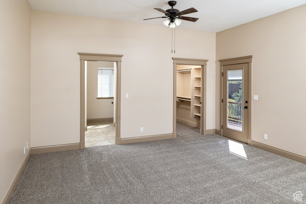 Unfurnished bedroom featuring light colored carpet, ceiling fan, access to outside, a closet, and a walk in closet