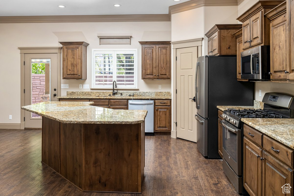 Kitchen with appliances with stainless steel finishes, a kitchen island, crown molding, dark wood-type flooring, and light stone counters