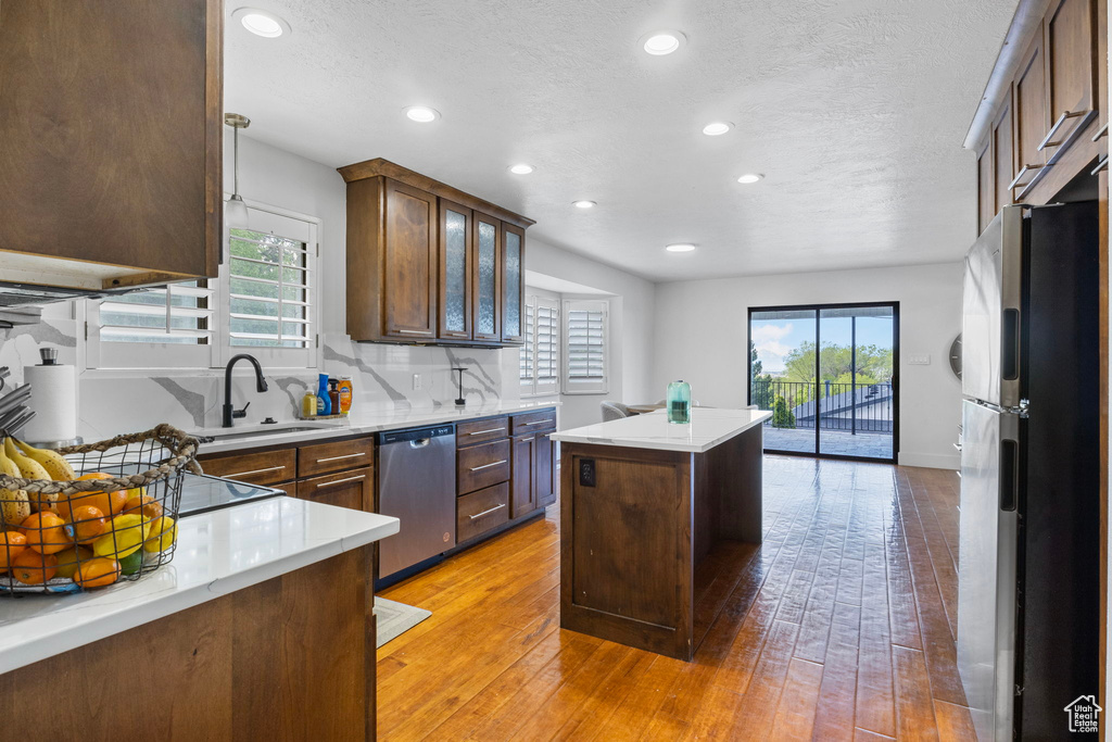 Kitchen featuring appliances with stainless steel finishes, a center island, sink, tasteful backsplash, and hardwood / wood-style flooring