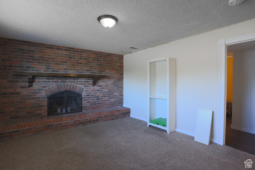 Unfurnished living room featuring brick wall, dark carpet, a textured ceiling, and a fireplace