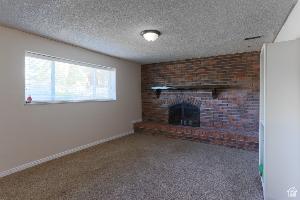 Unfurnished living room with a textured ceiling, carpet floors, brick wall, and a brick fireplace