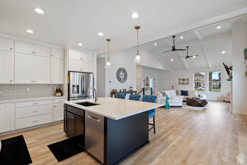 Kitchen featuring appliances with stainless steel finishes, a kitchen island with sink, lofted ceiling with beams, white cabinetry, and light wood-type flooring