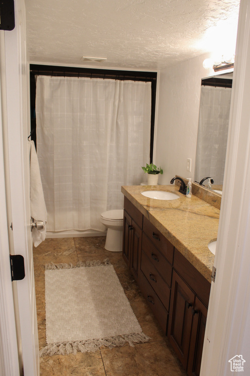 Bathroom featuring a textured ceiling, toilet, dual vanity, and tile flooring