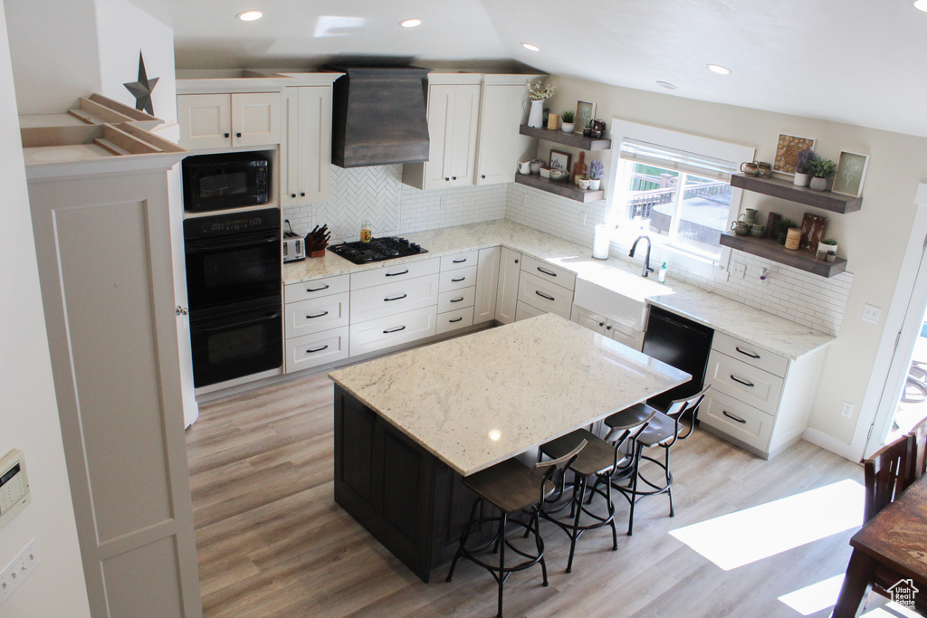 Kitchen with lofted ceiling, tasteful backsplash, custom exhaust hood, and black appliances